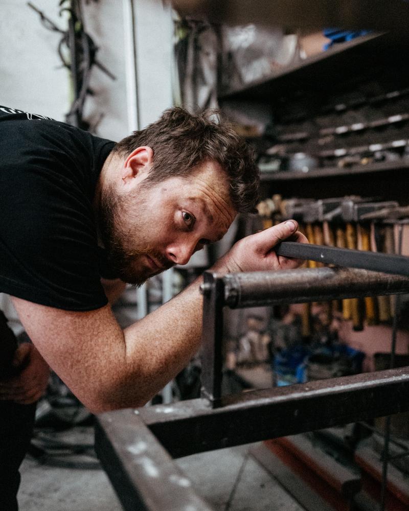 Metal worker inspecting rod as it is fired in oven