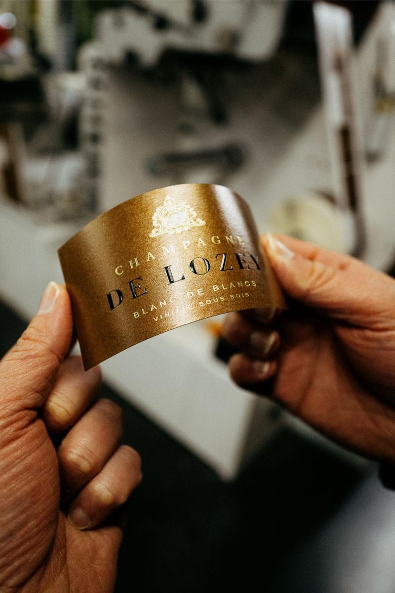 Pair of hands holding Champagne De Lozey Blanc des Blancs vinifié sous bois label at print shop