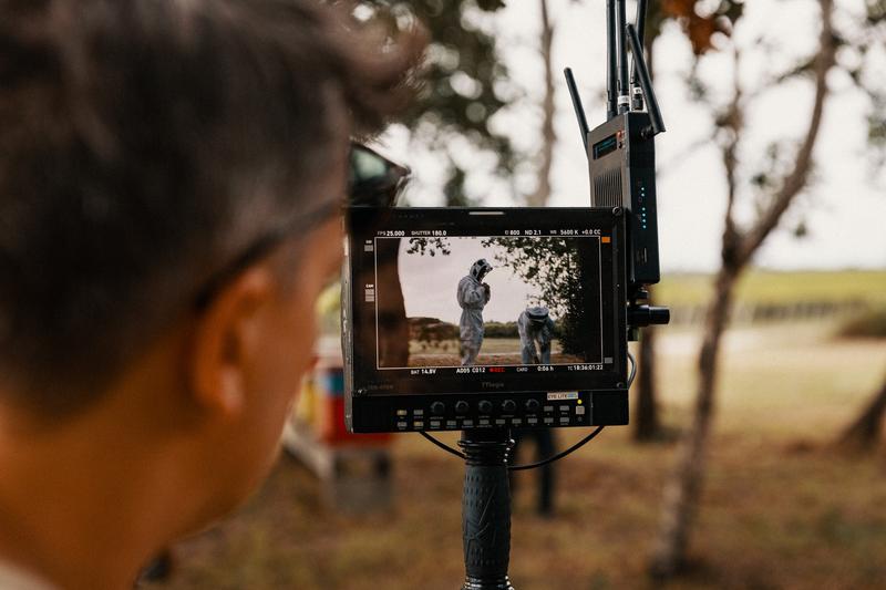 Man looking through video monitor at two men putting on beekeeping overalls