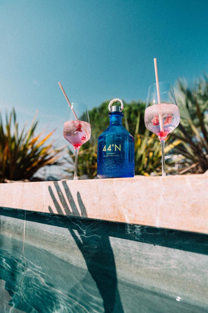 Bottle of Gin 44 on side of swimming pool with two cocktails either side and hand shadow