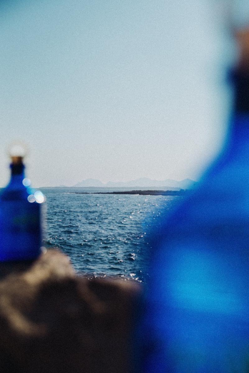 Two bottles of Gin 44 out of focus sitting on rocks in front of Mediterranean sea