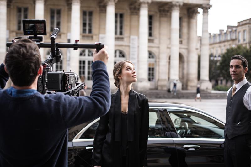 Backstage photo of man filming doorman helping girl getting out of a car in front of Bordeaux Grand Theatre