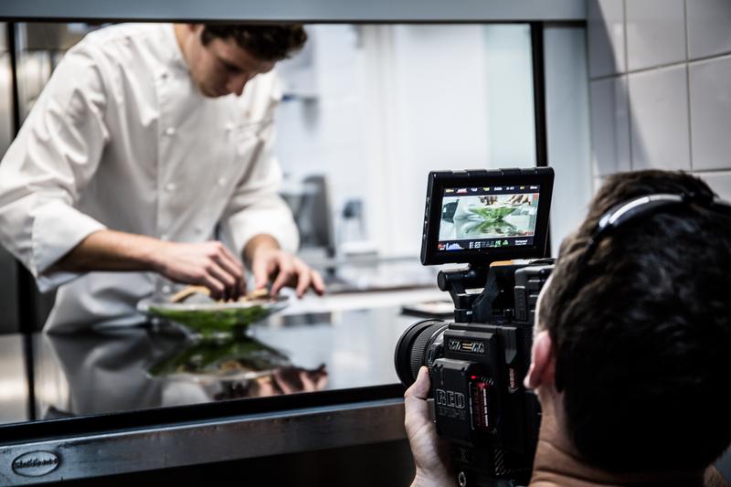 View from behind of man filming patisserie chef preparing dessert