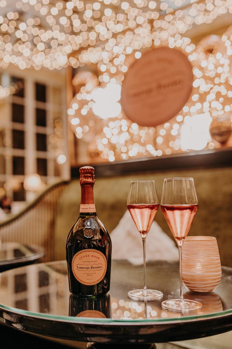 Bottle of Laurent Perrier rosé and two glasses on table surrounded by christmas lights