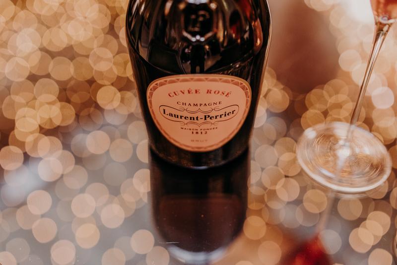 Close up of bottle of Laurent Perrier rosé on glass table with reflections of christmas lights
