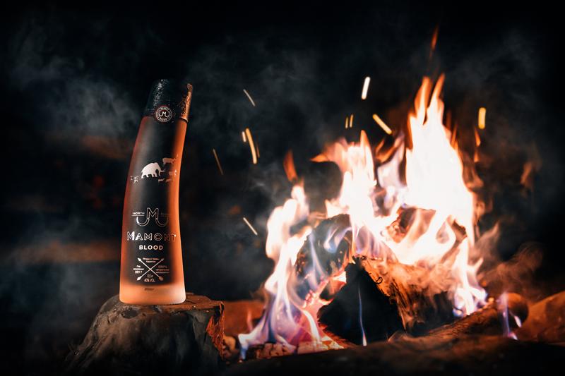 Bottle of Mamont Blood vodka sat on treestump next to roaring campfire