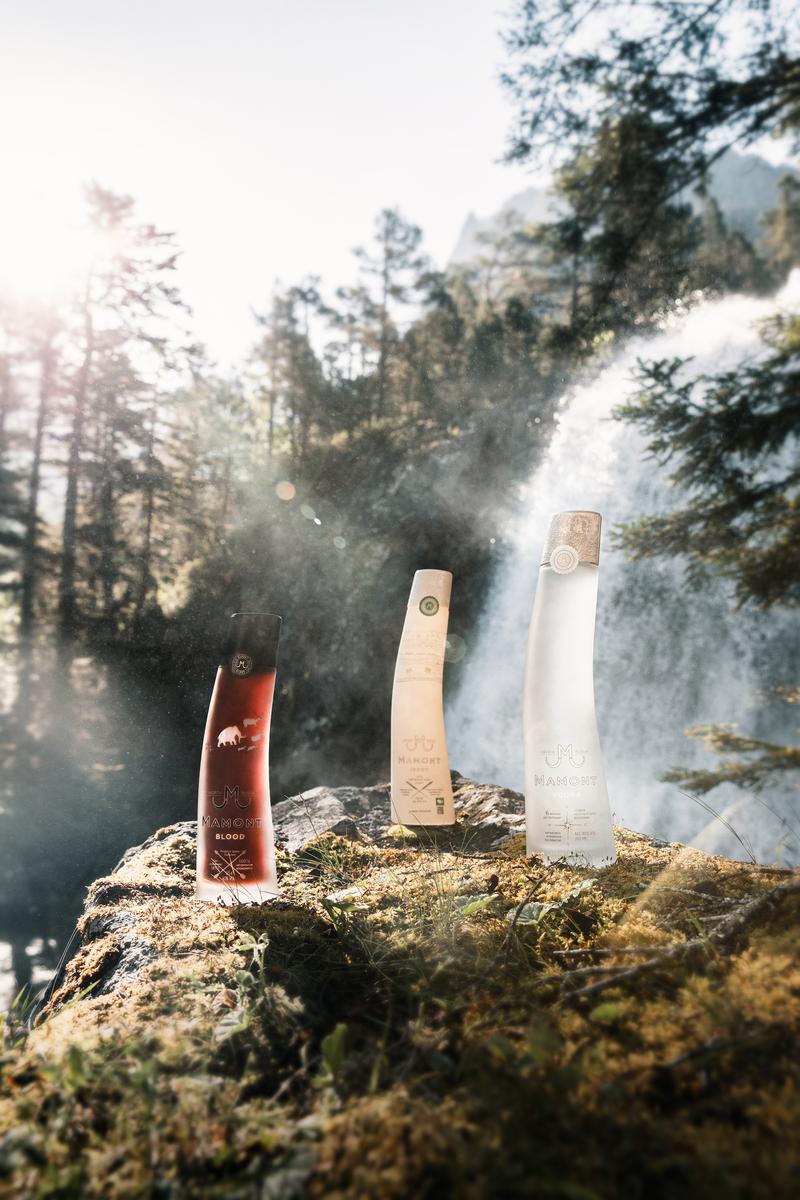 Full range of Mamont Vodka bottles sat on rock in front of waterfall