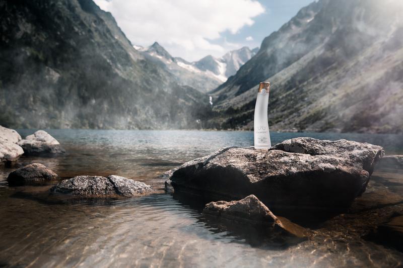Landscape of bottle of Mamont vodka sitting on rock next to lake in the mountains