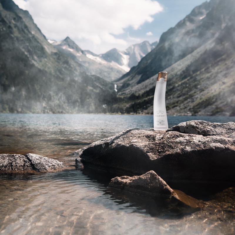 Landscape of bottle of Mamont vodka sitting on rock next to lake in the mountains