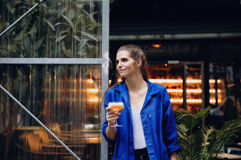 Portrait of Juliette Larrouy holding cocktail in front of Le Syndicat bar