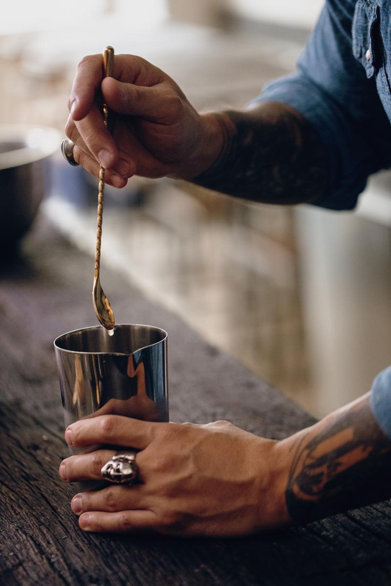 Close up of hands stirring a cocktail using a spoon and cocktail shaker