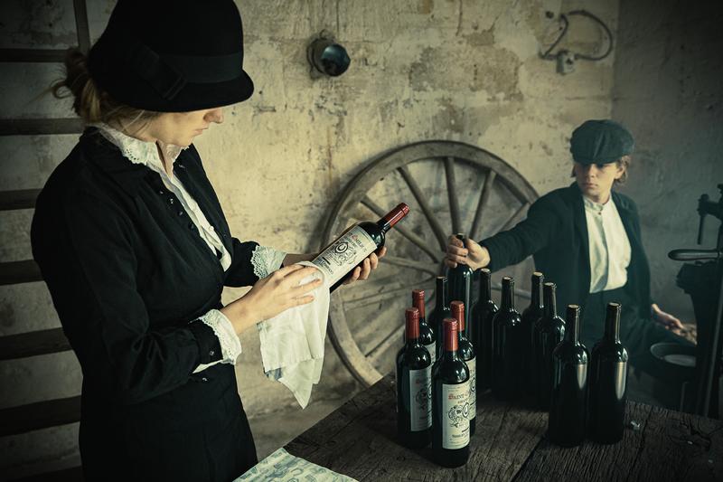 Woman labelling bottles for the Shelby Company with boy in background using corking machine