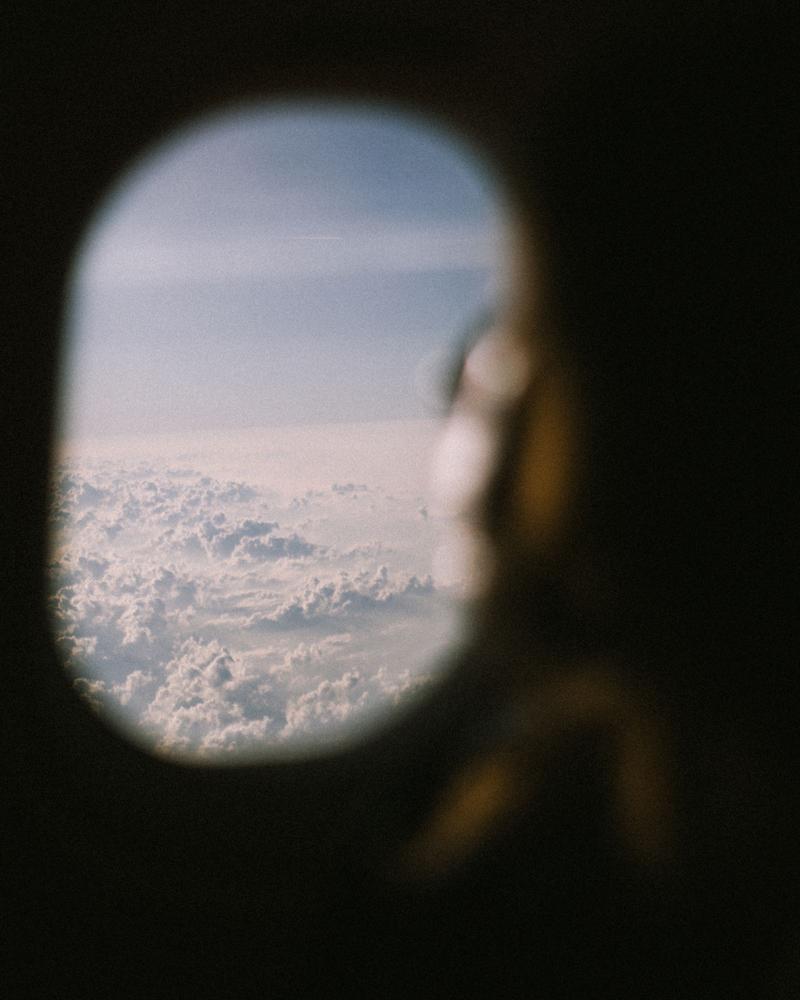 View out of window of aeroplane showing fluffy clouds and out of focus head silhouette