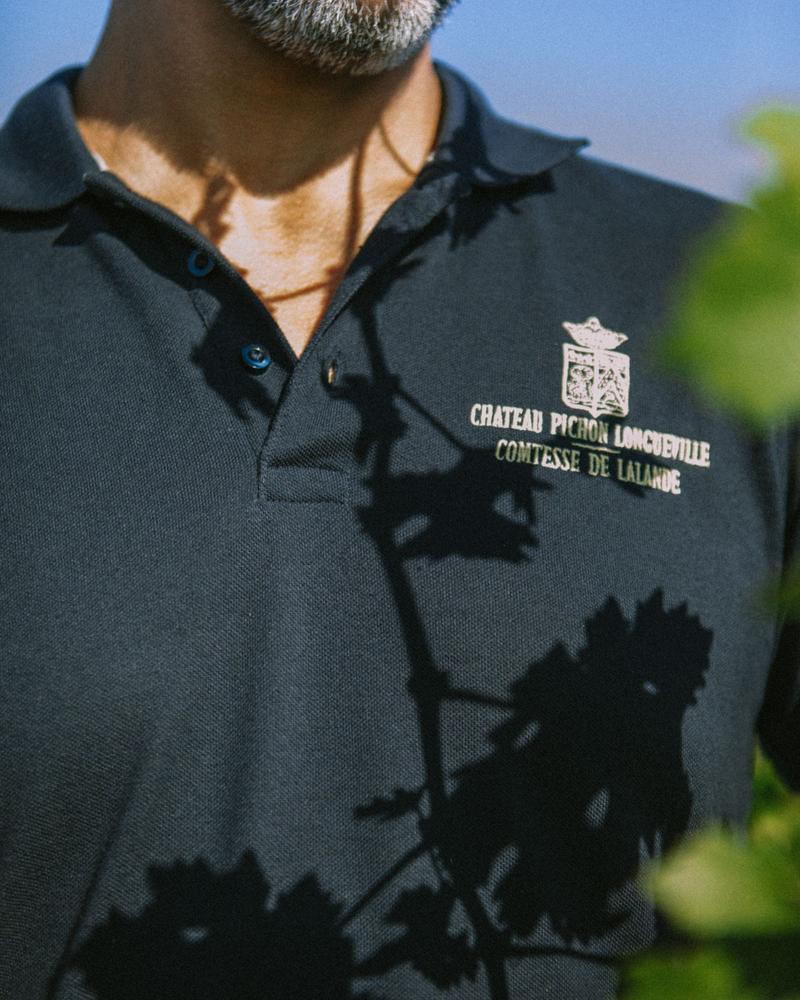 Shadow of vines projected onto polo shirt of vineyard worker showing chateau Pichon Comtesse logo