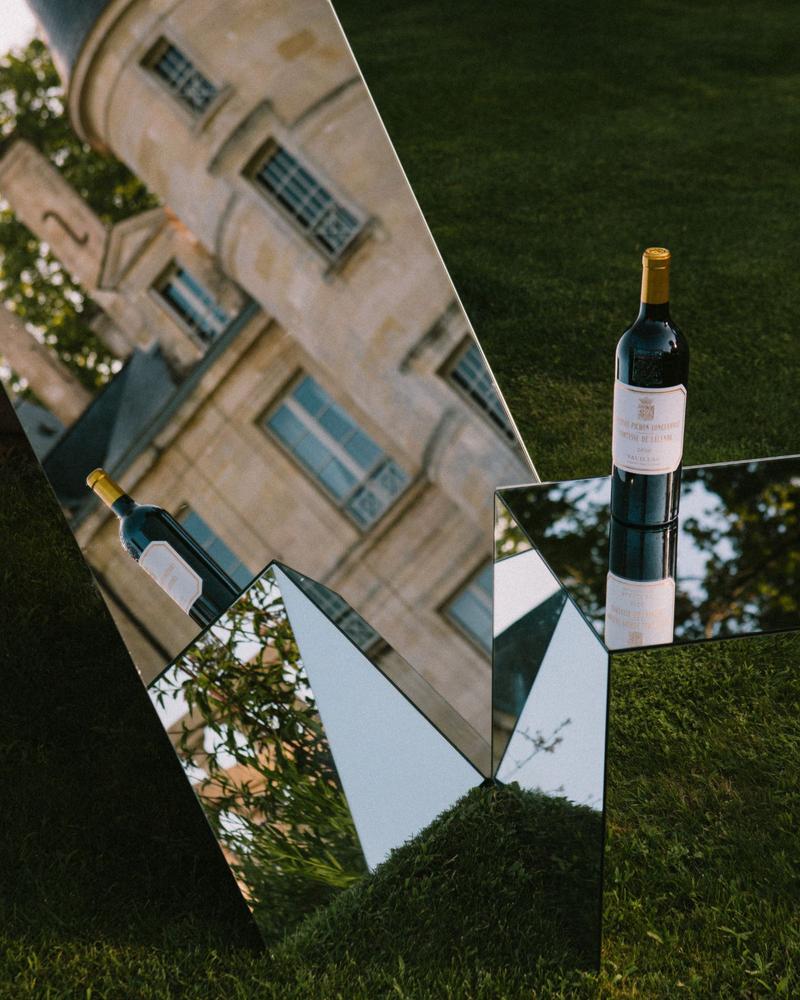 Bottle of Chateau Pichon Comtesse sat on top of mirror cube showing reflections of surrounding gardens.