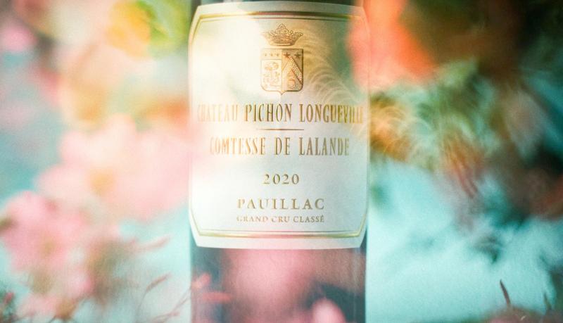 Bottle of Pichon Comtesse surrounded by blurred pink flowers on a blue background