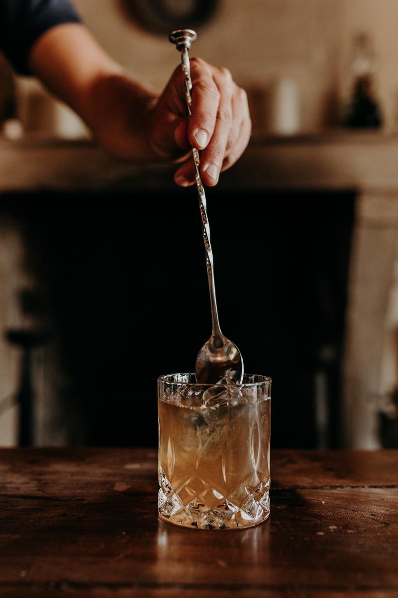 Hand using long spoon to stir St-Rémy cocktail