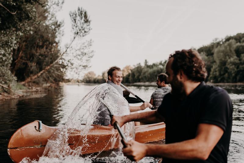 Boy using canoe paddle to splash friends in another canoe