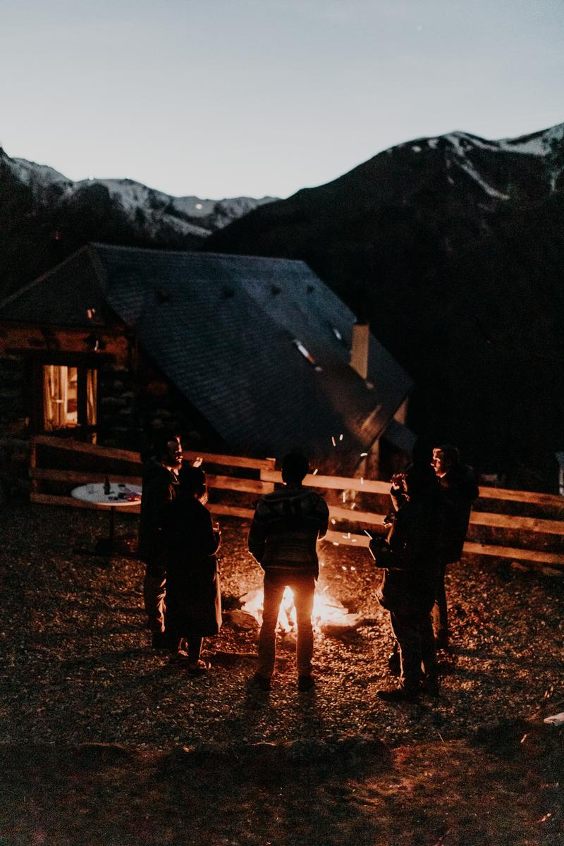 Group of friends by fireside in front of mountain cottage at night