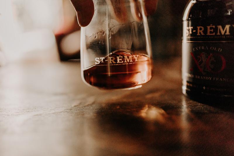 Close up of hand swirling glass of brandy above table showing St-Rémy logo